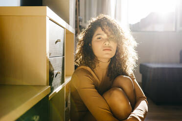 Portrait of attractive young woman sitting on the floor at home in sunlight - TCEF00418