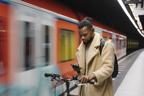 Stilvoller Mann mit Fahrrad und Smartphone in einer U-Bahn-Station - AHSF02112