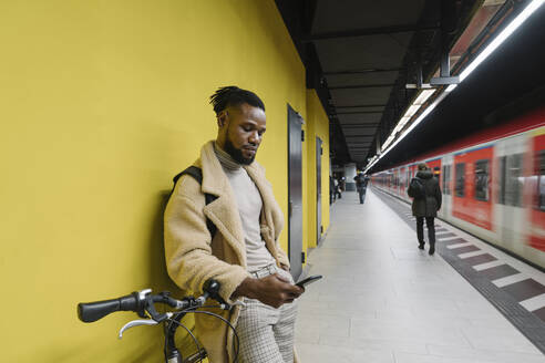 Stilvoller Mann mit Fahrrad und Smartphone in einer U-Bahn-Station - AHSF02113