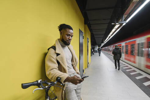 Stylish man with a bicycle and smartphone in a metro station - AHSF02113
