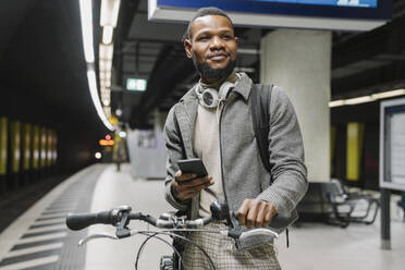 Stilvoller Mann mit Fahrrad, Kopfhörer und Smartphone in einer U-Bahn-Station - AHSF02120