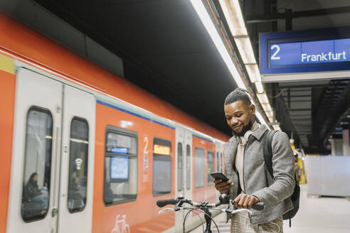 Stilvoller Mann mit Fahrrad, Kopfhörer und Smartphone in einer U-Bahn-Station - AHSF02121