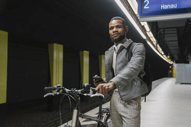 Stilvoller Mann mit Fahrrad, Kopfhörer und Smartphone in einer U-Bahn-Station - AHSF02123