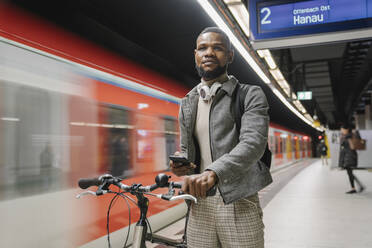 Stilvoller Mann mit Fahrrad, Kopfhörer und Smartphone in einer U-Bahn-Station - AHSF02124