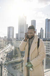 Stilvoller Mann am Telefon auf einer Aussichtsterrasse mit Blick auf ein Hochhaus, Frankfurt, Deutschland - AHSF02129