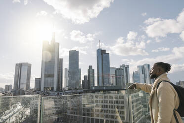 Stilvoller Mann auf einer Aussichtsterrasse mit Blick auf einen Wolkenkratzer, Frankfurt, Deutschland - AHSF02130