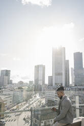 Stylish man using smartphone on observation terrace with skycraper view, Frankfurt, Germany - AHSF02133