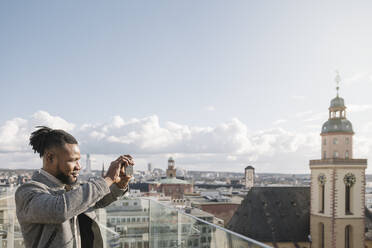 Stilvoller Mann auf der Aussichtsterrasse beim Fotografieren mit dem Handy, Frankfurt, Deutschland - AHSF02135