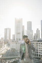 Stilvoller Mann am Telefon auf einer Aussichtsterrasse mit Blick auf ein Hochhaus, Frankfurt, Deutschland - AHSF02141