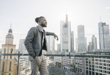 Stilvoller Mann auf einer Aussichtsterrasse mit Blick auf einen Wolkenkratzer, Frankfurt, Deutschland - AHSF02144