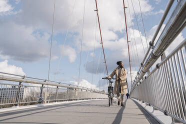 Stylish man with a bicycle walking on the bridge - AHSF02150