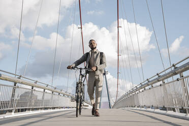 Stylish man with a bicycle walking on a bridge - AHSF02151
