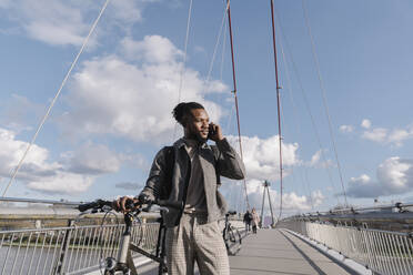 Stilvoller Mann mit Fahrrad, der auf einer Brücke telefoniert - AHSF02153