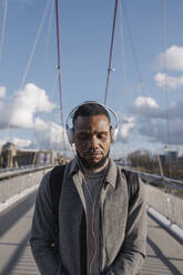 Portrait of stylish man on a bridge with headphones listening to music with closed eyes - AHSF02156