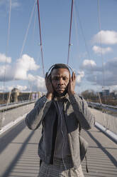 Portrait of stylish man on a bridge with headphones listening to music - AHSF02157