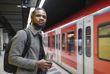 Stilvoller Mann mit wiederverwendbarem Becher und Kopfhörern in einer U-Bahn-Station - AHSF02160