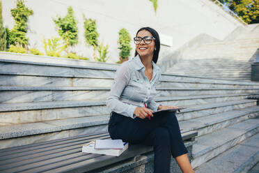 Geschäftsfrau mit Klemmbrett sitzt auf einer Bank in einem Park - OYF00112