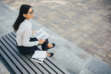 Geschäftsfrau mit Klemmbrett sitzt auf einer Bank in einem Park - OYF00113