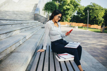 Businesswoman using smartphone sitting on a bench in a park - OYF00118