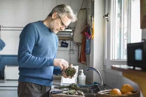 Mature man preparing artichokes in his kitchen - MCVF00252