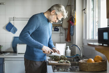 Älterer Mann bereitet Artischocken in seiner Küche zu - MCVF00253