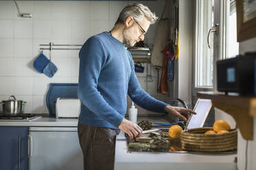 Älterer Mann bereitet Artischocken in seiner Küche mit einem digitalen Tablet zu - MCVF00256