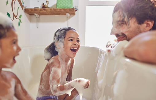 Verspielte Töchter in der Badewanne wischen Seifenblasen auf das Gesicht des Vaters - CAIF25483