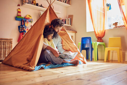 Vater und kleine Tochter lesen ein Buch im Tipi - CAIF25486