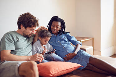 Young pregnant family using smart phone on living room sofa - CAIF25500