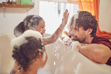 Playful daughters in bubble bath wiping bubbles on father’s face - CAIF25515