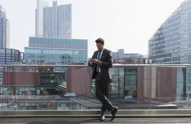 Geschäftsmann mit Smartphone auf sonnigem Balkon, Shoreditch, London - CAIF25552