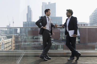 Businessmen talking on sunny, urban balcony, Shoreditch, London - CAIF25600