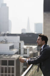 Thoughtful businessman on sunny, urban balcony - CAIF25669