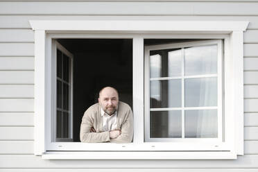 Porträt eines reifen Mannes, der sich aus dem Fenster seines Hauses lehnt - VYF00116