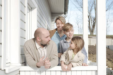 Happy family talking on porch of their house - VYF00125