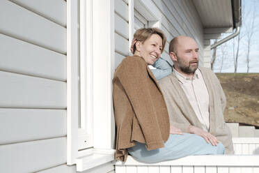 Glückliches Paar im Gespräch auf der Veranda ihres Hauses - VYF00126