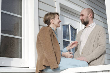 Glückliches Paar im Gespräch auf der Veranda ihres Hauses - VYF00127
