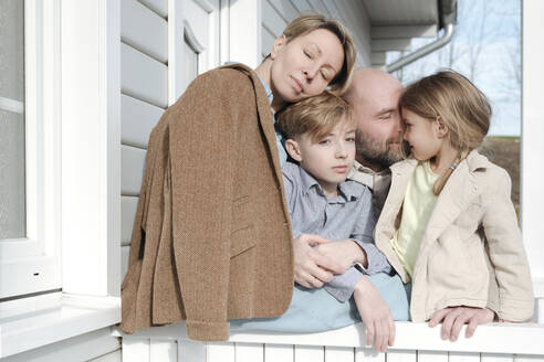 Glückliche Familie, die sich vor ihrem Haus umarmt - VYF00130