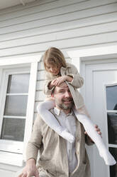 Portrait of father with happy daughter on his shoulders in front of their house - VYF00135