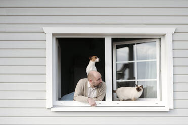 Älterer Mann mit Katze und Hund lehnt sich aus dem Fenster seines Hauses - VYF00143