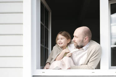 Älterer Mann mit lächelnder Tochter schaut aus dem Fenster ihres Hauses - VYF00144