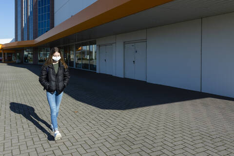Mädchen mit Maske läuft draußen vor einem geschlossenen Einkaufszentrum, lizenzfreies Stockfoto