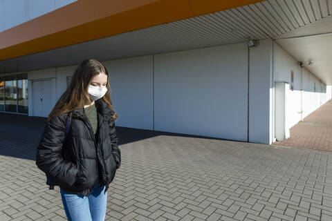 Mädchen mit Maske läuft draußen vor einem geschlossenen Einkaufszentrum, lizenzfreies Stockfoto