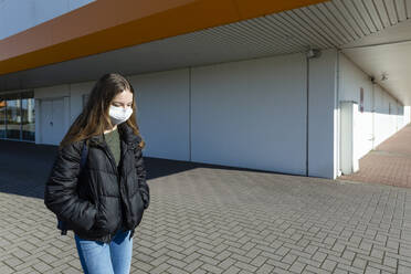 Mädchen mit Maske läuft draußen vor einem geschlossenen Einkaufszentrum - OJF00365