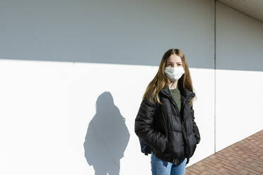 Mädchen mit Maske vor einer weißen Wand stehend - OJF00369