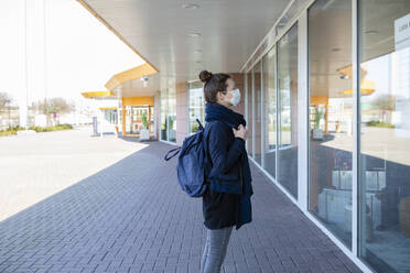 Woman with mask standing in front of a display window of closed shopping center - OJF00374