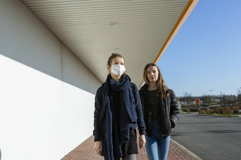 Woman wearing face mask walking with daughter at an empty street - OJF00377