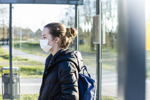 Porträt eines Mädchens mit Maske, das an der Bushaltestelle wartet, lizenzfreies Stockfoto