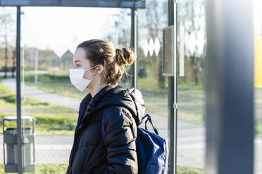 Porträt eines Mädchens mit Maske, das an der Bushaltestelle wartet - OJF00381