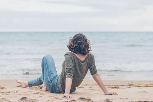 Junge Frau sitzt am Strand und blickt auf das Meer - FVSF00016